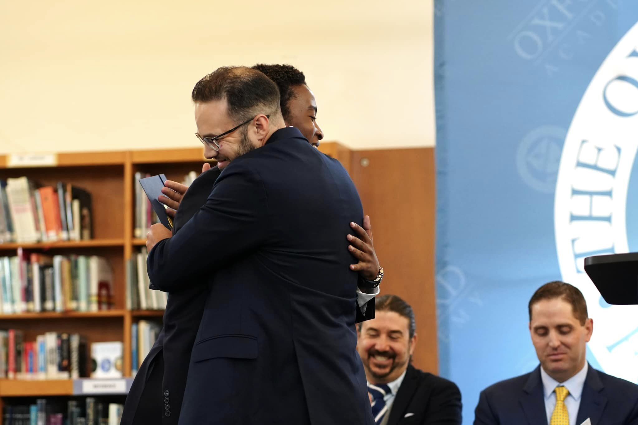 A man in a suit is hugging a man in a suit at The Best Boarding School.